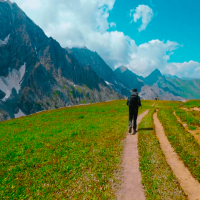 A breathtaking view of the serene Vishansar Lake, surrounded by lush green meadows and snow-capped peaks, captured during the Kashmir Great Lakes Trek. The clear blue sky reflects on the pristine waters, creating a perfect mirror image of the majestic mountains.
